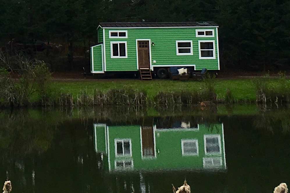 Striking green outside of the Retro Southern Charm custom tiny house, shown here reflecting in a lake